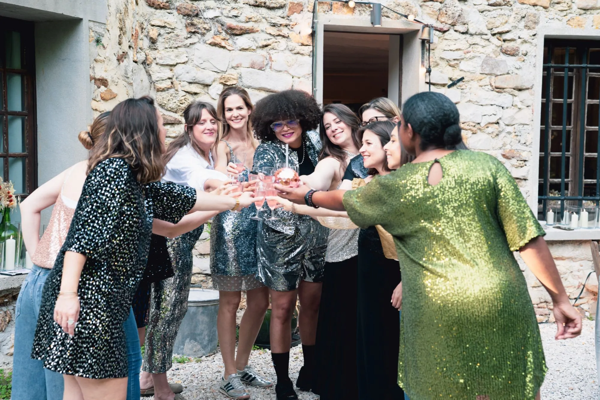 Les participantes en tenues à sequins trinquent ensemble devant une maison en pierre