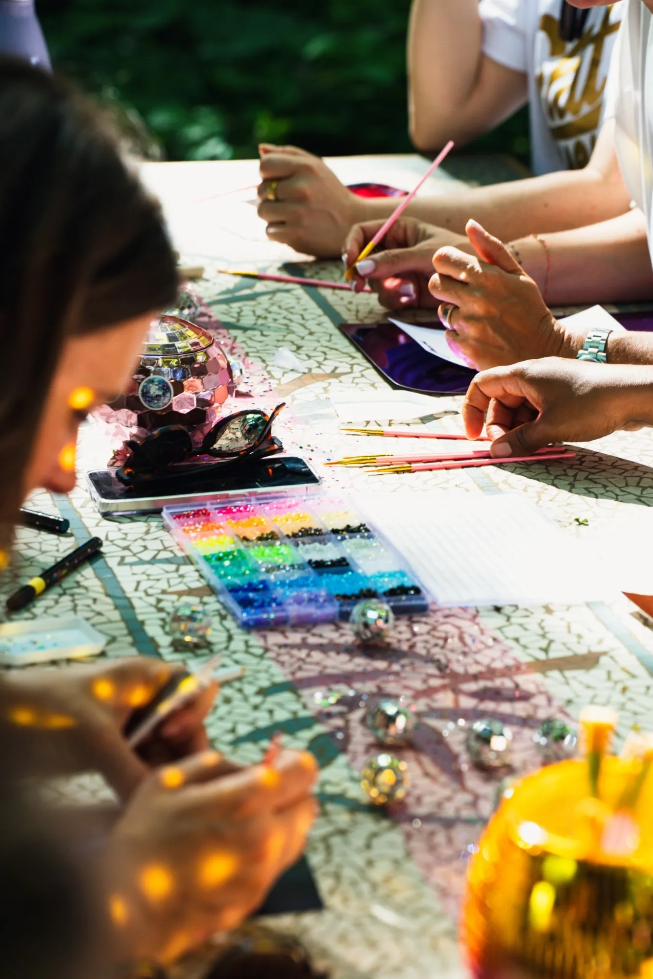 Gros plan sur l'atelier créatif, des mains qui posent des strass colorés au pinceau, entre petites boules à facettes