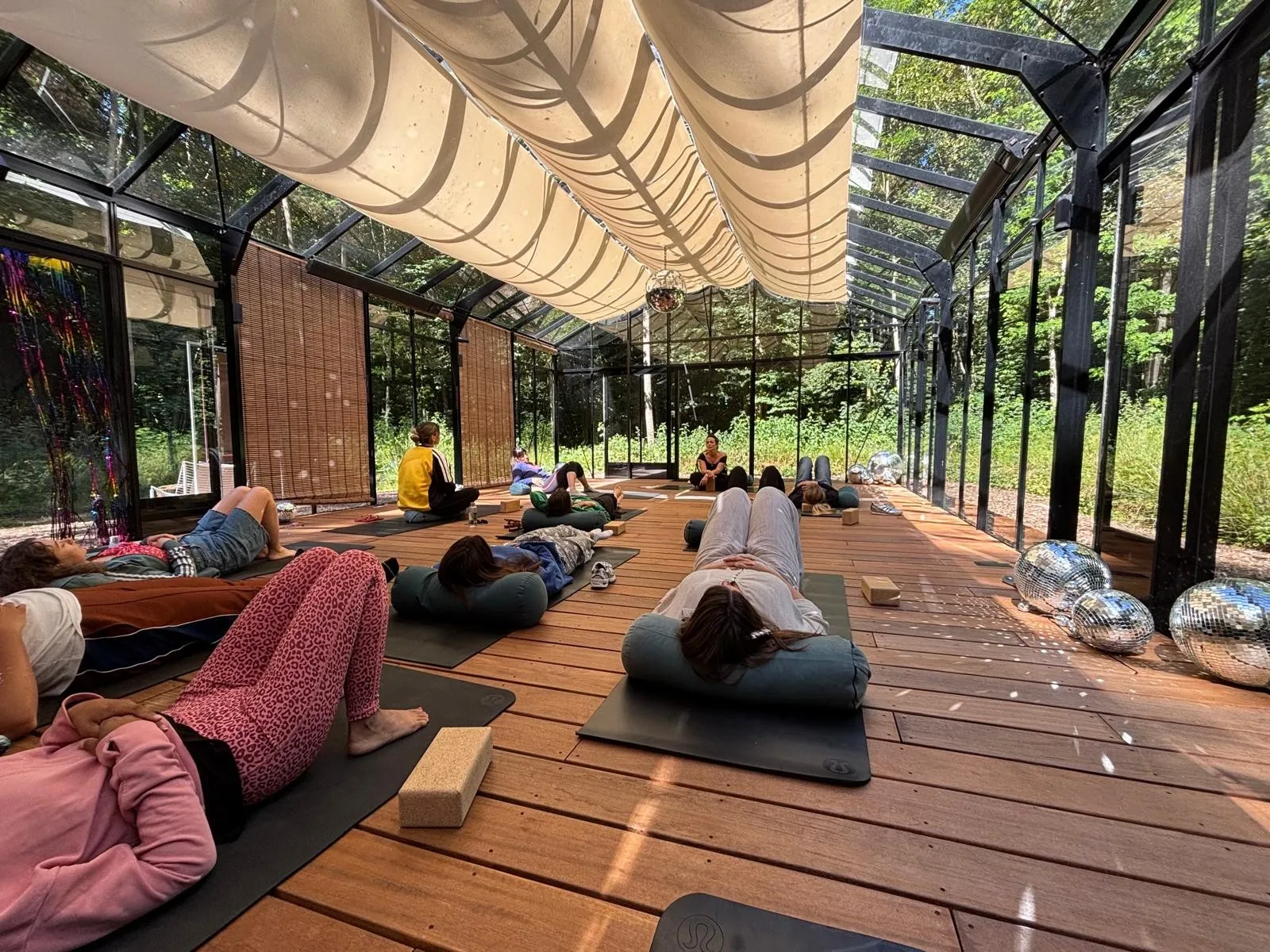 Temps de relaxation, les participantes allongées sur leurs tapis dans la verrière ouverte sur la forêt, entourées de boules à facettes