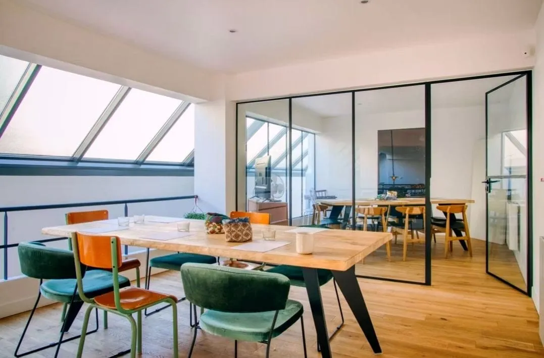Salle lumineuse sous verrière à l'étage, grande table en bois et chaises vertes