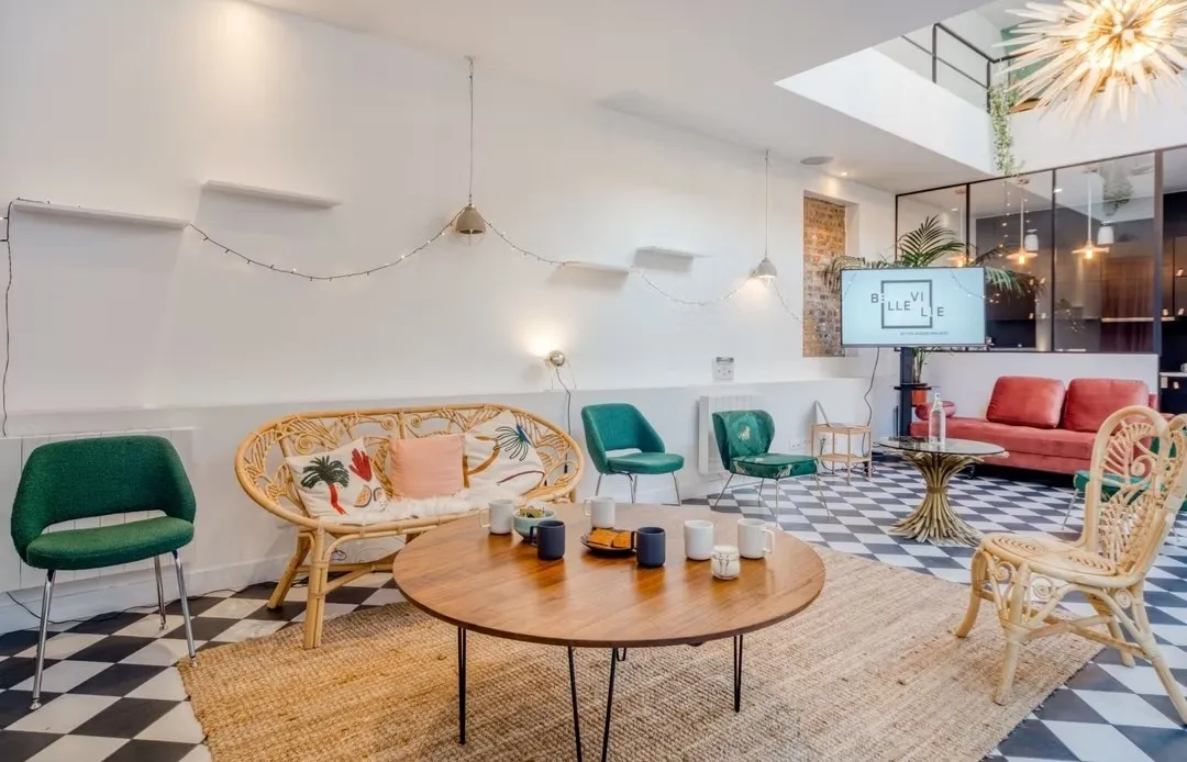 Le salon de la Maison Boson, sol en damier noir et blanc, fauteuils verts, banquette en rotin et table basse en bois